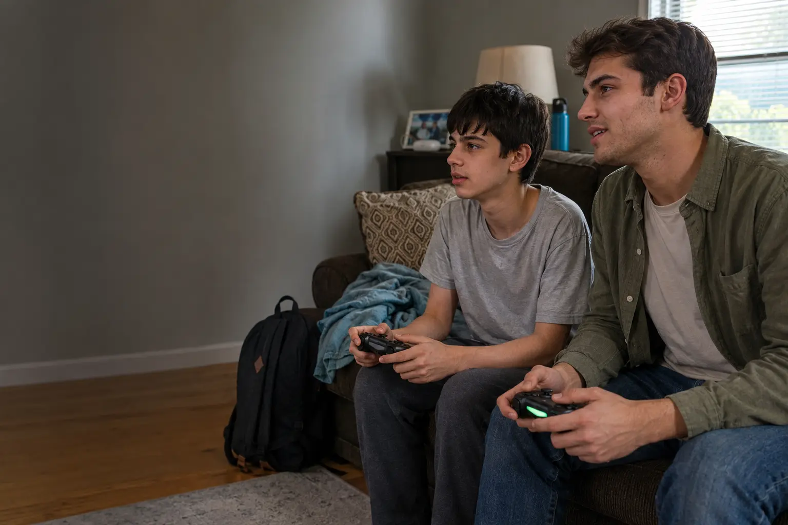 A teenage boy playing a video game beside his college-age male Care Specialist in a family living room