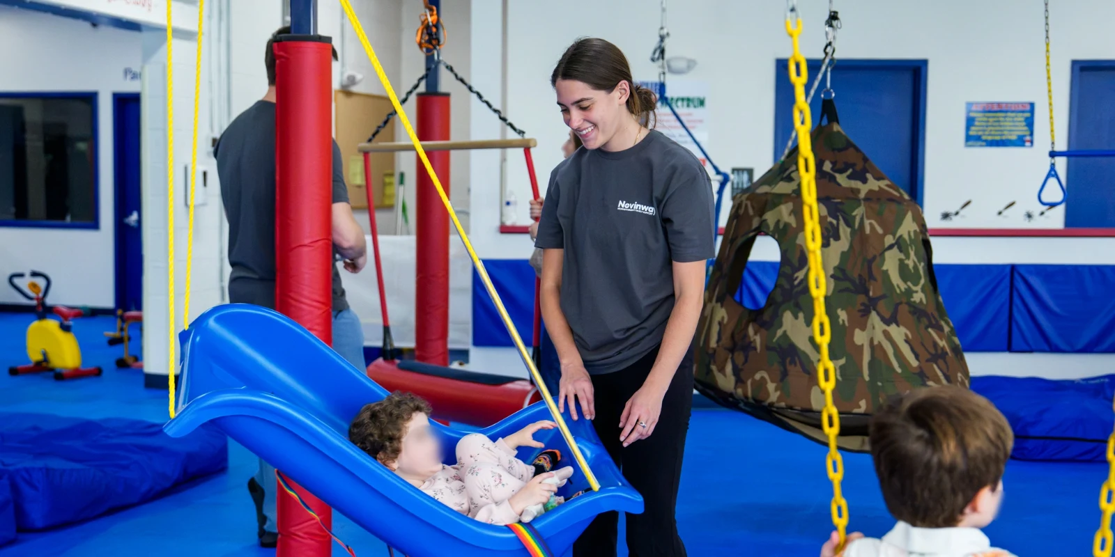 A Care Specialist smiling down at a toddler riding a bucket swing