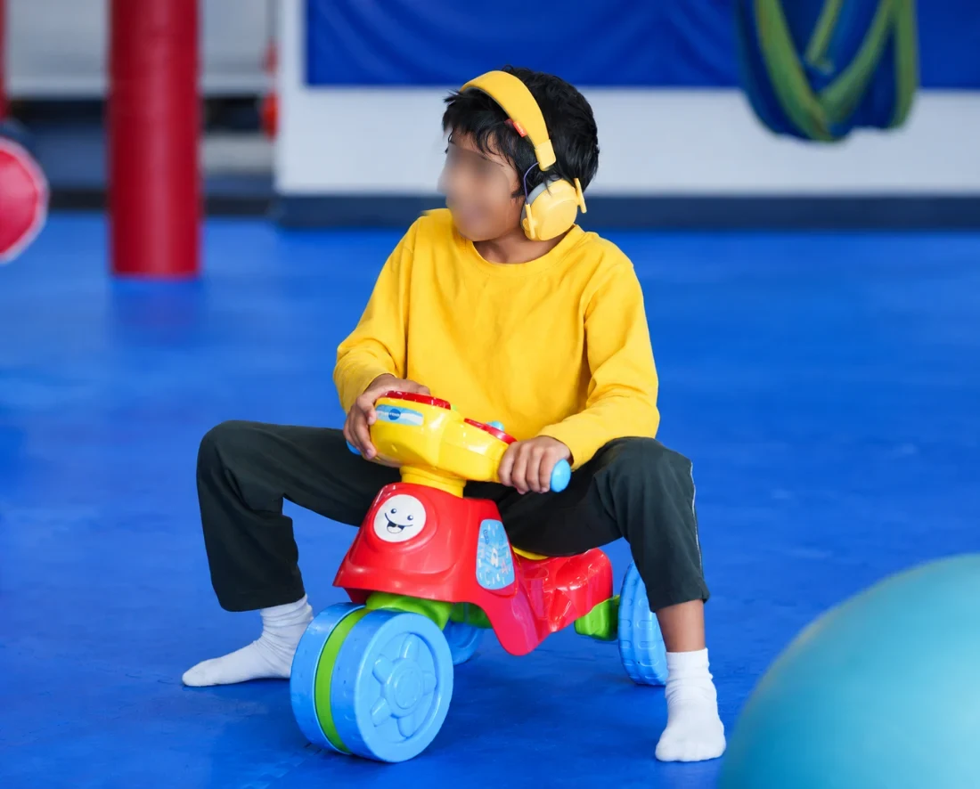 A boy in yellow noise-reducing headphones riding a toy trike at We Rock the Spectrum Gaithersburg