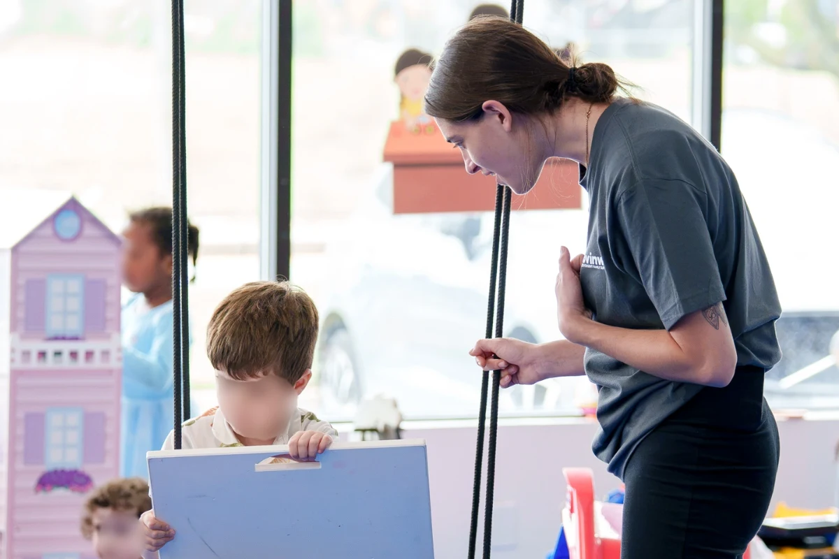 A Care Specialist leaning in to talk with a boy sitting on a swing