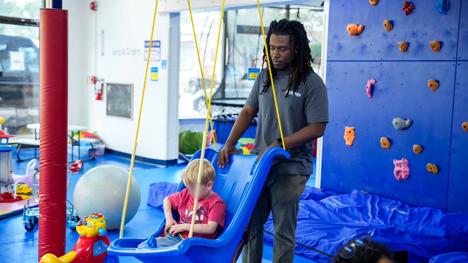 A Care Specialist steadying a boy on a platform swing