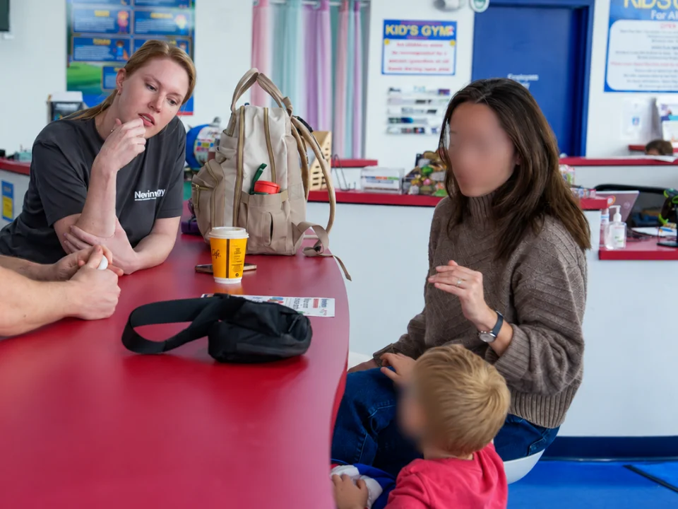 Sydney listening as a parent talks through her questions at a table, with her toddler beside her