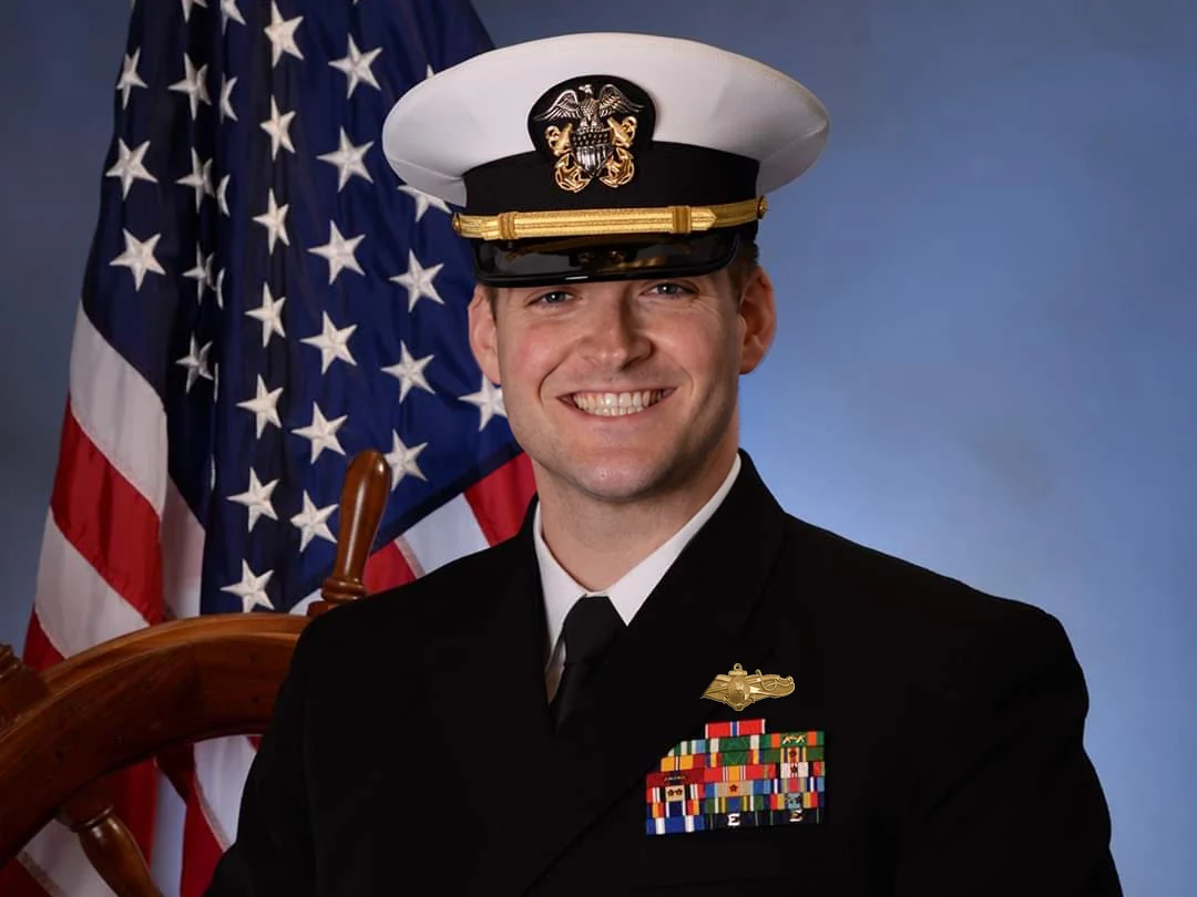 Jeff Moeller in Navy service dress blues with lieutenant’s insignia, seated before an American flag and a ship’s wheel