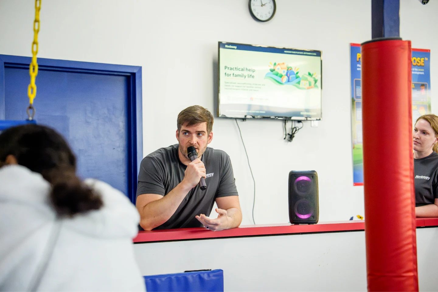 Jeff Moeller speaking into a microphone at the event, a Novinway slide on the screen behind him