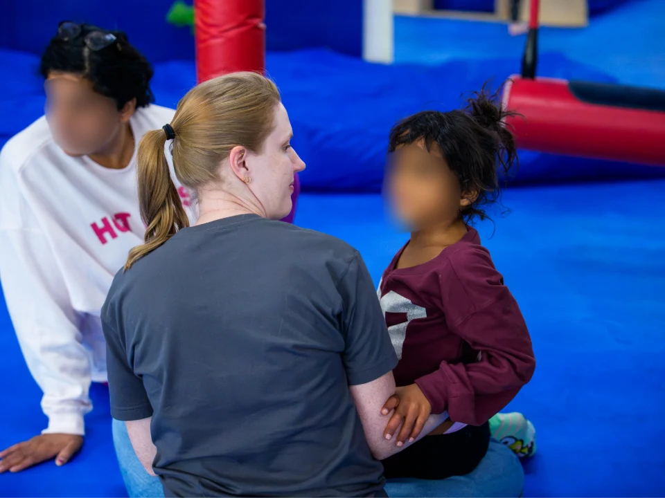 Sydney Pickard sitting on a gym mat beside a young girl who holds her arm