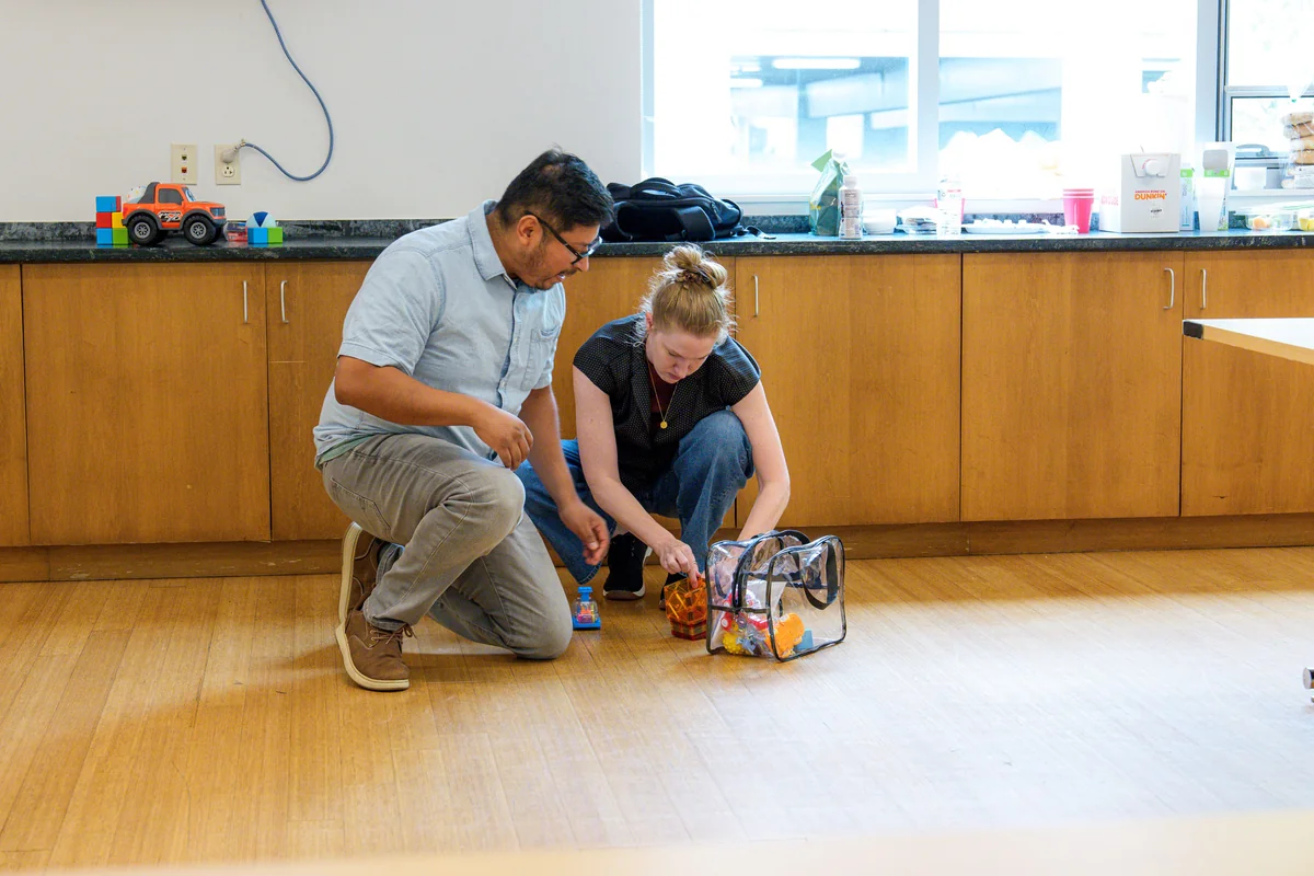 Two people kneeling on the floor beside a clear bag of toys during Care Specialist training