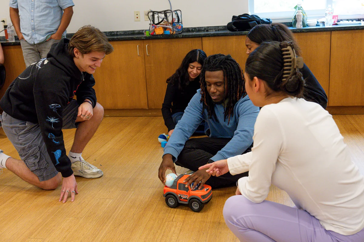 Care Specialists kneeling on the floor, practicing play with a toy car during training